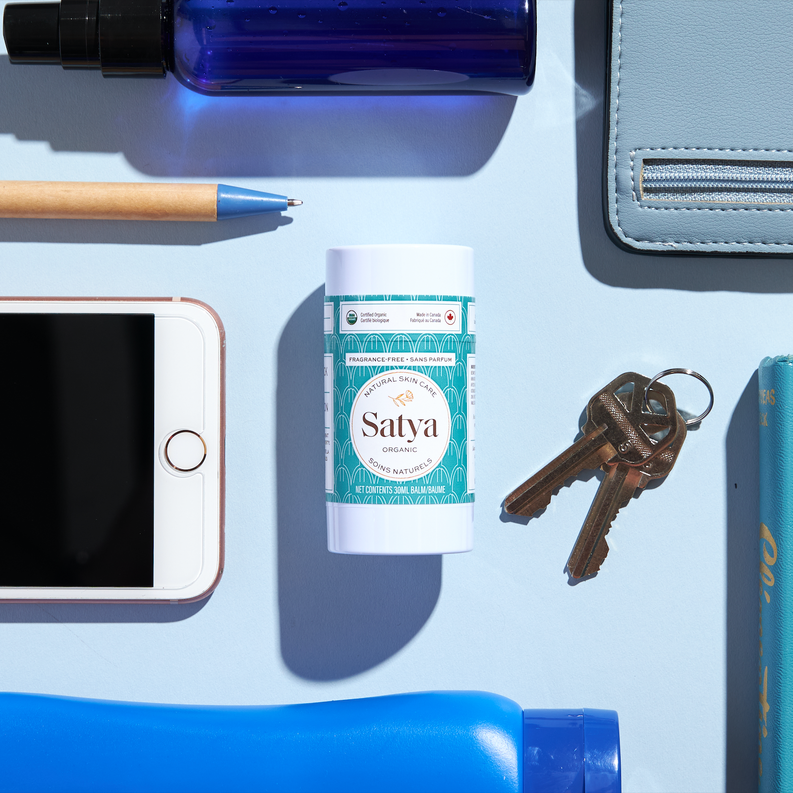 Satya Multi Use Easy Glide Stick surrounded by items used daily, such as keys, a phone, a pen, a water bottle, and a bag.